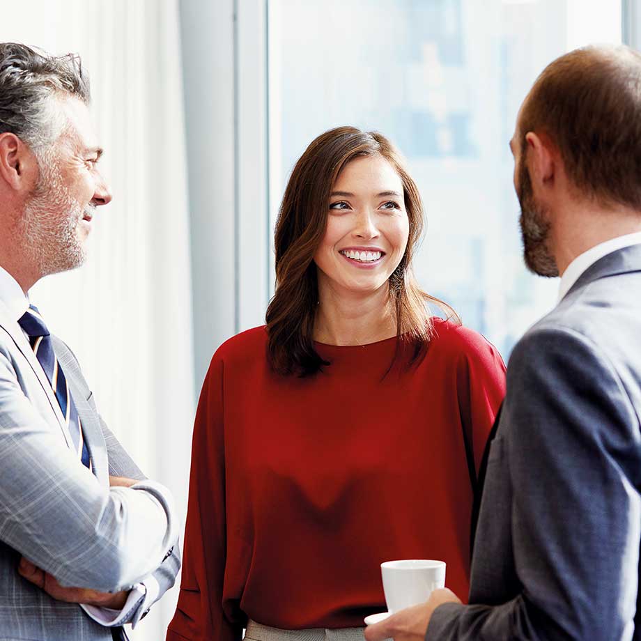 Two men in suits chatting to a lady wearing a red jumper
