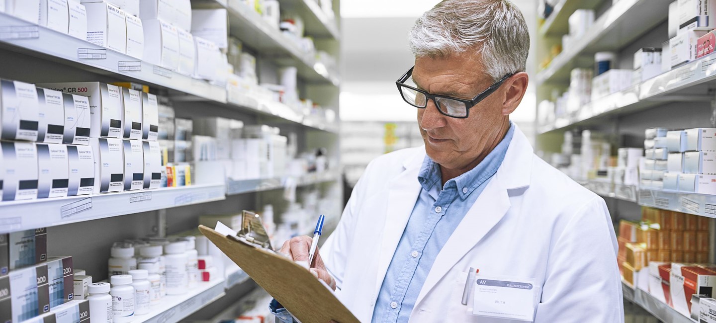 PHARMACIST, IN PHARMACY, TAKING NOTES ON A CLIPBOARD