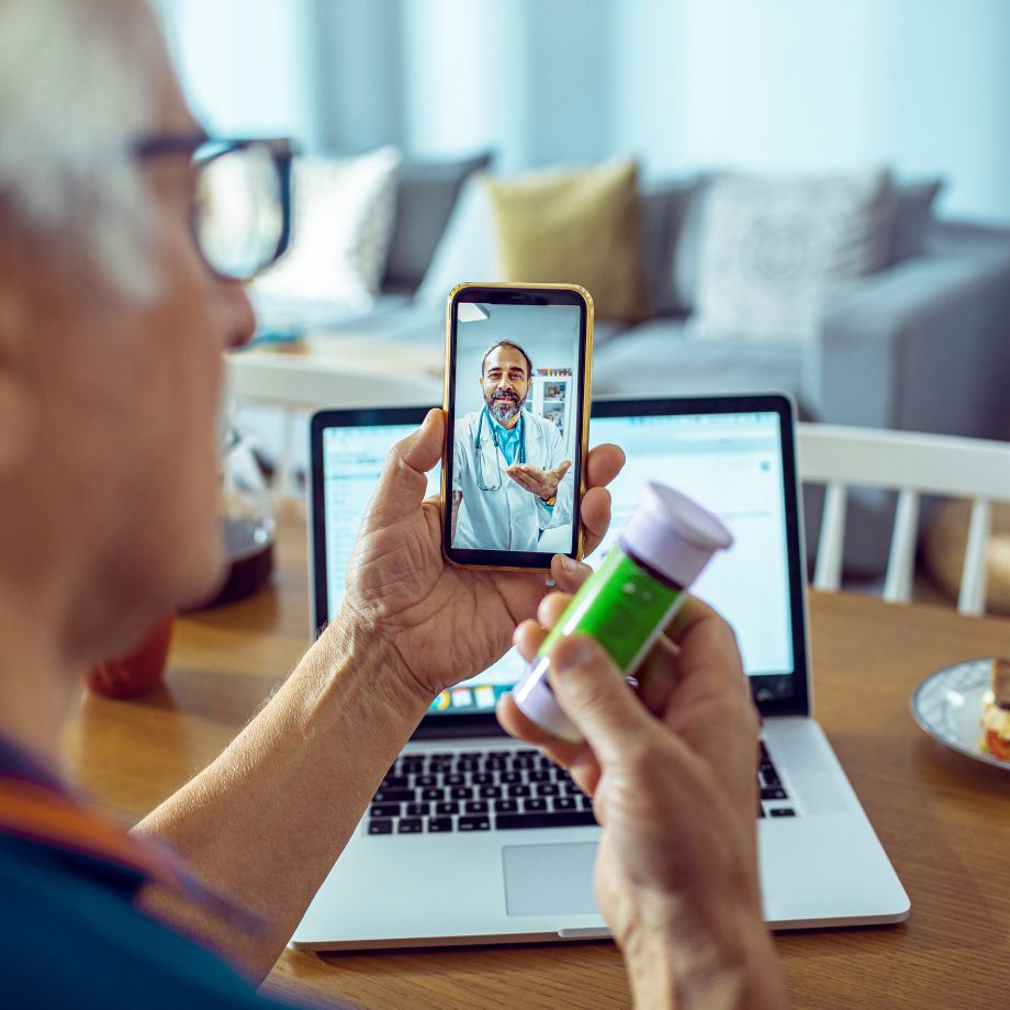 Patient holding a pill bottle and talking to a doctor through video call on his cell phone.
