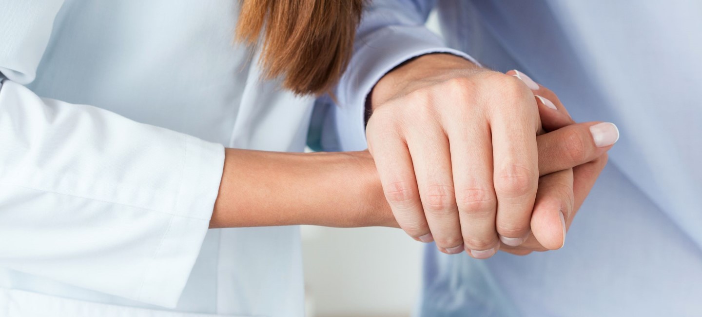Doctor and patient holding hands as a sign of support.